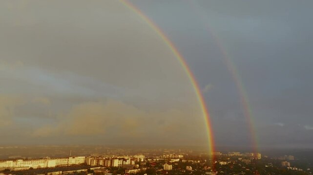 Two rainbows intertwine beautifully in the cloudy sky and at the end of their tail they blur as if touching the big buildings of the city.