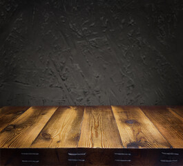  An empty wooden countertop against a black, dark concrete wall. Home interior. Evening, dim light. Space for text. Copy space
