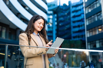 Successful businesswoman using a digital tablet while standing in front of business office building. Young businessperson, professional occupation worker, modern technology developer on urban street.