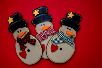Three decorative snowmen with colorful hats and scarves on a bright red background during the festive winter season