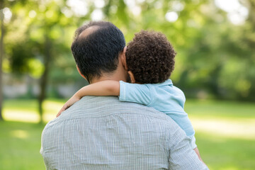 A father lovingly embraces his young child in a serene park during a sunny afternoon