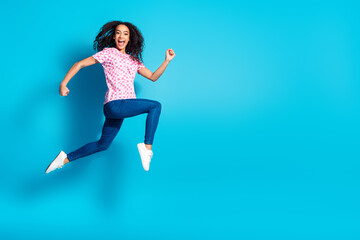 Full length photo of adorable lovely girl wear print t-shirt jumping high running empty space isolated blue color background