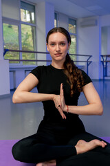 close up in studio of spiritual development master class on yoga girl with long hair on a purple mat sits lotus pose in hand tree bell meditation folded hands