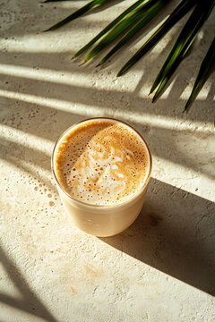 Iced Latte coffee in a health-focused, chic cafe with lush fronds, off-white decor, natural shadows, boujee, bougie, fair trade, eco vibe