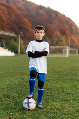 Young football player in white uniform posing on football field. School sports club.