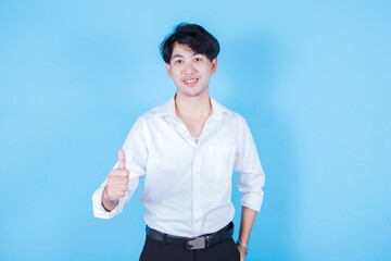 Asian man guy wearing smiles at the camera while showing his thumbs up. Half body portrait on blue background.