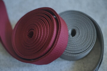 
A close-up of two rolls of fabric webbing in maroon and beige, unspooling on a soft gray background. This detailed shot is perfect for showcasing texture and material for crafts, fashion, and DIY the