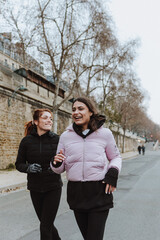 Two French girls or hispanic couple of women in sports outfit stretching and doing exercises outdoors in winter weather in Europe