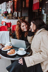 French business couple of women friends working and using laptop at coffee shop in winter in an urban city in Europe, cold weather 