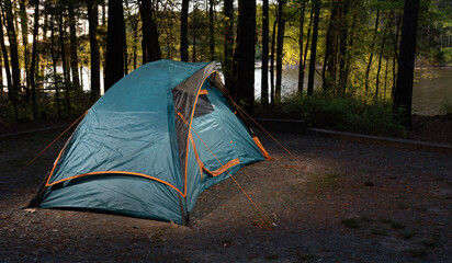 Orange trim on a blue backpacking tent pitched at a campsite in the forest with the water of a lake visible behind.
