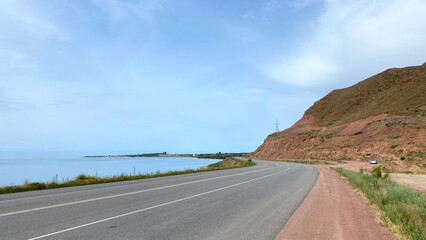 The ring road around Lake Issyk-Kul in Kyrgyzstan, Asia. Beautiful mountain summer landscape. View of an empty paved road in the early morning. Trekking and hiking in Kyrgyzstan