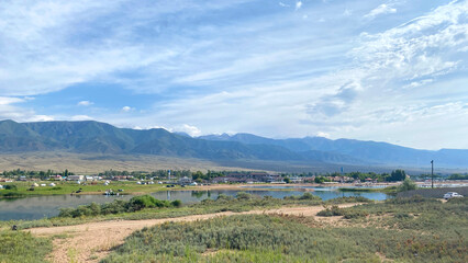 Obraz premium View of a small backwater of the Issyk-Kul mountain lake in Kyrgyzstan, Asia. Rural landscape. Beautiful summer panorama of a small village in the mountains of Kyrgyzstan. Travel and tourism