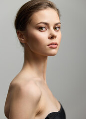 Elegant young woman with a natural expression, showcasing minimal makeup and a sleek hairstyle against a soft gray background. Beauty and fashion concept.