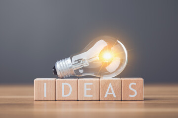 Light bulb next to wooden letters spelling 'IDEAS' arranged on a table symbolizes the spark of new ideas and creativity. This image reflects inspiration and the pursuit of innovative thinking