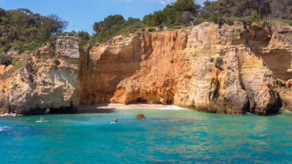 Fototapeta premium A couple paddles together on a stand-up board in Algarve’s blue ocean near scenic cliffs