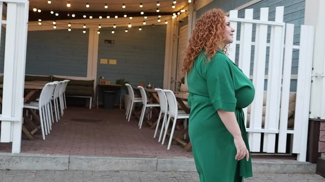 Beautiful Plus size Woman with Curly Red Hair Smiles at Camera, Walking on street with Blurred Bokeh Background of Warm Lights Outdoors