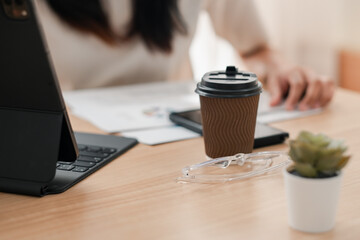 A modern workspace featuring a coffee cup, glasses, and tablet on a wooden desk, ideal for remote work or study.