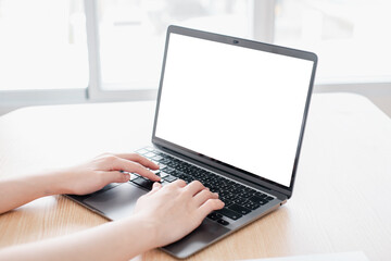 Close-up of hands typing on a laptop with a blank screen in a bright, modern office environment.