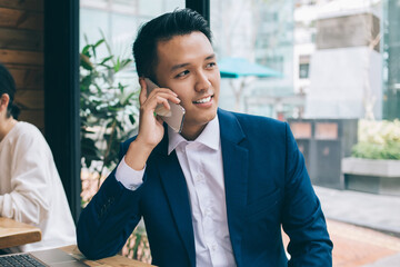 Asian young smiling businessman sitting and talking on phone
