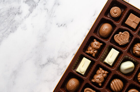 Top view of assorted chocolate candies in a box on marble background with copy space. 