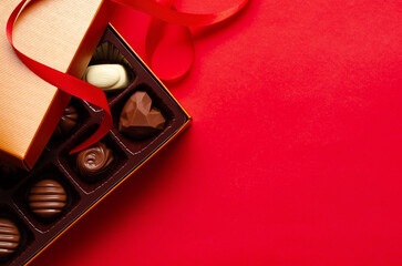 Assorted chocolate candies in a golden box and a red ribbon, on red background with copy space. 
