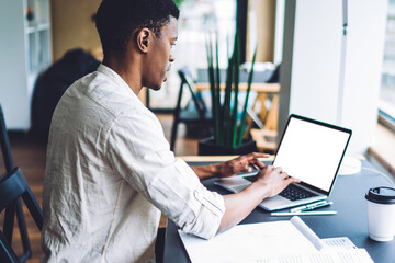 Dark skinned male freelancer working remotely on modern laptop computer with blank screen for internet web advertising, millennial student preparing to exam with web information from netbook