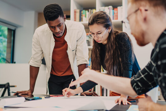 Male and female colleagues brainstorming at desktop table in coworking space developing creative strategy for college course work, multicultural hipsters discussing ideas during knowledge learning