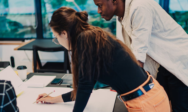 Millennial group of diverse developers creating architect project using blueprint sketch at table desktop indoors, progressive youth discussing ideas for university education during learning process