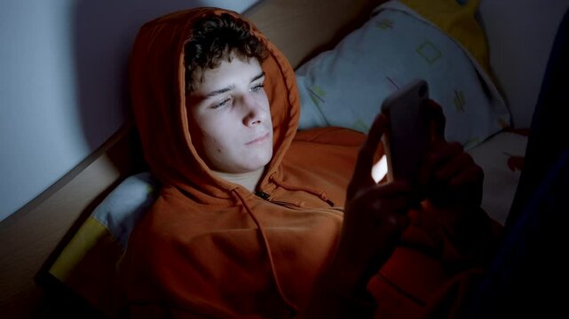 4k medium handheld shot of teenager using a smartphone lying in bed late at night, playing games, watching videos, and scrolling the screen.Children's screen addiction.Screen Addiction in Youth