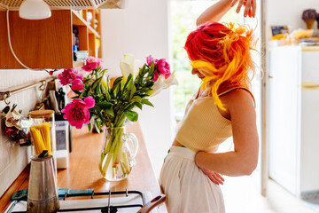 Young woman dancing joyfully in bright kitchen with flowers
