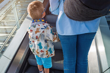 child and adult legs on an escalator at Alkmaar train station, with the child wearing a dinosaur-patterned jacket and blue shorts, capturing everyday movement.