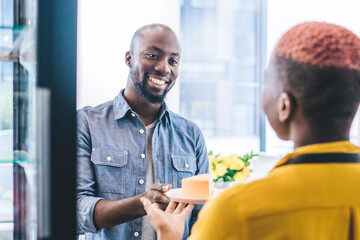 Cheerful black customer getting plate with cake from hand of barista