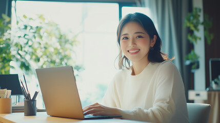 若くてかわいいアジア人女性が、デスクでパソコン作業をしている。笑顔のビジネスシーンの撮影。