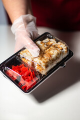 Sushi to go concept. Take away box with sushi rolls in woman hands in gloves. Food delivery concept. Take away food concept.