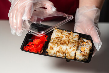 Woman in gloves packaging sushi in plastic box. Plastic containers for food delivery. Using plastic for packaging. Food in disposable dishes.