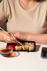 Female eating sushi with chopstiks at home. Tasty asian food concept. Sushi rolls in take away package. Delivery concept.
