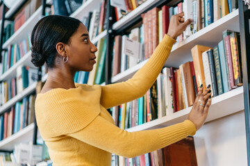 Focused ethnic student picking book from bookcase