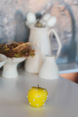 A unique Easter-themed decoration featuring a bright yellow apple adorned with small pearls, creating a playful and artistic centerpiece on a simple white surface.