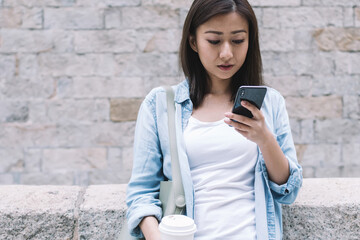 Pretty Asian woman texting and holding coffee