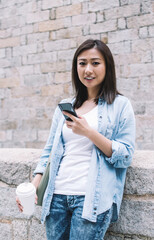 Modern Asian calm casual woman using smartphone on street