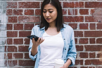 Asian woman using smartphone and drinking coffee on street