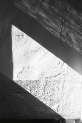 Obraz premium Black and white photo of sunlight creating geometric shadows on a textured white wall, showcasing minimalist design.