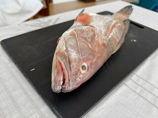 A photo of gutted and cleaned grouper fish on a cutting board. Preparing a Mediterranean delicacy, seafood.