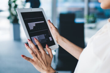 Focused businesswoman in glasses standing and working with graphics on tablet