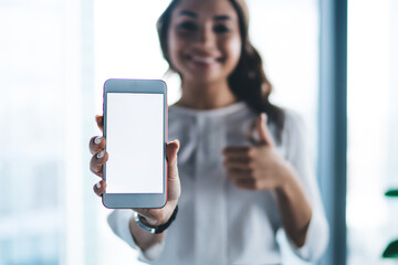Pretty smiling female office worker showing smartphone in office