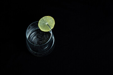 szklana szklanka wody mineralnej z plasterkiem cytryny na czarnym tle