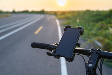 Smartphone and holder attached to the handlebar, riding a bicycle in the countryside with sunset in the sky