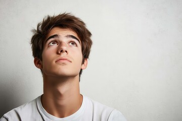 Fototapeta premium Young man looking up, thoughtful expression. Perfect for illustrating concepts like hope, inspiration, or contemplation.