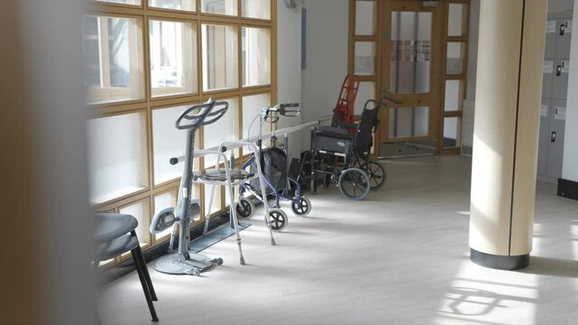 A room with a wheelchair and a walker. The room is empty and the wheelchair is in the middle of the room