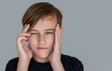 Little boy having a headache, pain. Headache child. Suffering migraine. Headache because stress. Portrait of a sad boy holding his head with his hand, isolated on the gray background